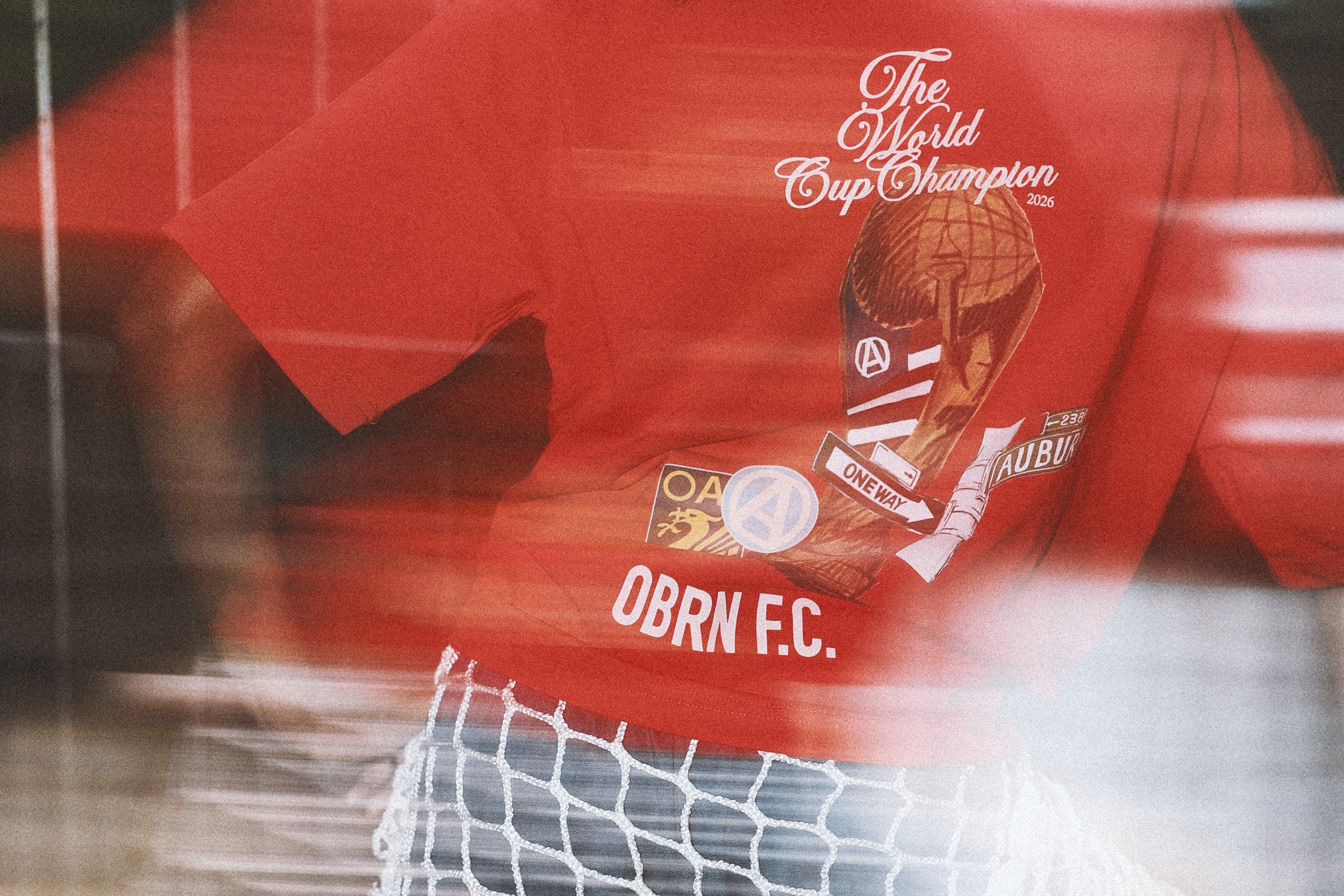 Person wearing a red sports jersey with branding and text, standing behind a net.
